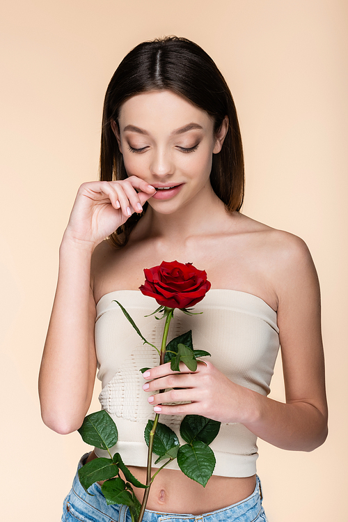 flirty woman with bare shoulders holding red rose isolated on beige