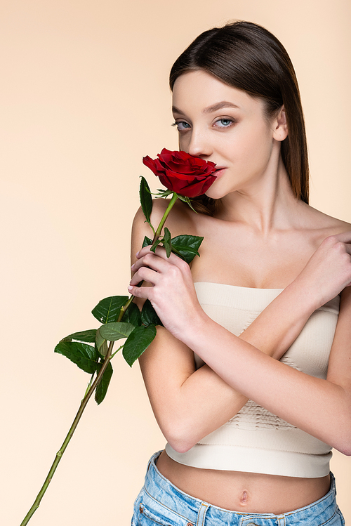 young woman with bare shoulders smelling aromatic rose isolated on beige