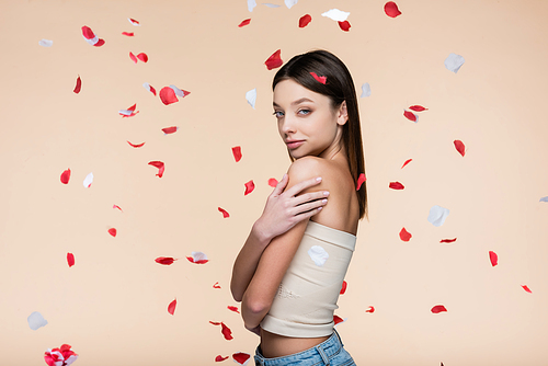 young woman in crop top near falling rose petals on beige