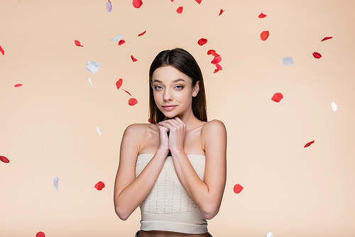 sensual young woman in crop top near falling rose petals on beige