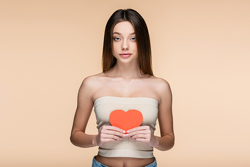 sensual woman in crop top with bare shoulders holding red paper cut heart isolated on beige