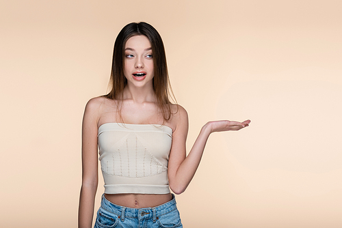 young and shocked woman in crop top pointing with hand isolated on beige