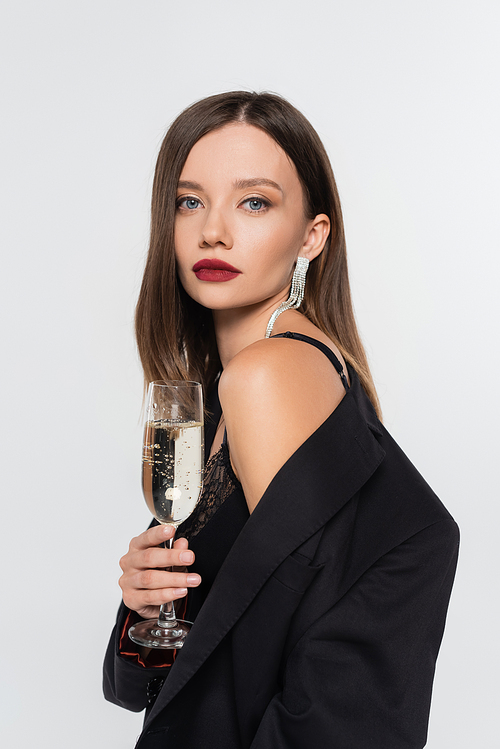 sexy brunette woman in black blazer  while holding glass of champagne isolated on grey