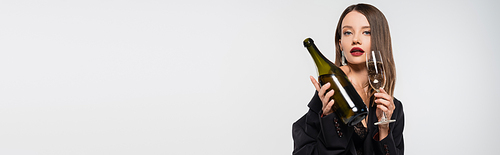 sensual woman in black blazer holding bottle and glass of champagne while  isolated on grey, banner