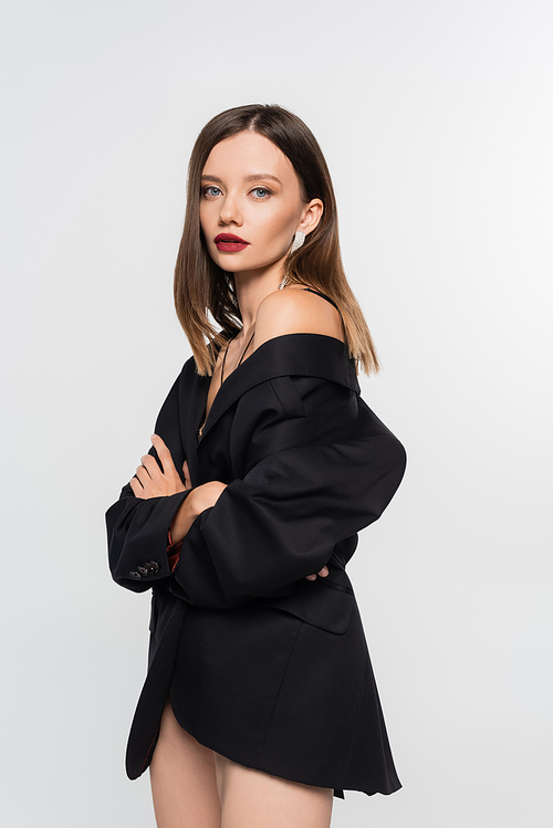 pretty brunette woman in black blazer, with naked legs, posing with crossed arms isolated on grey