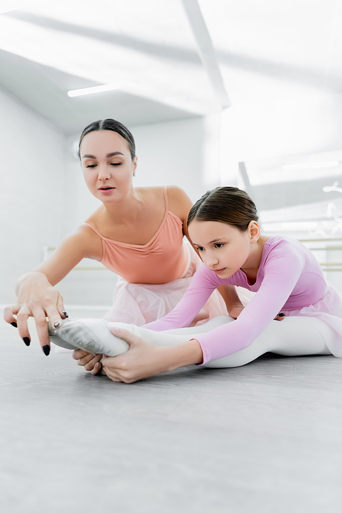 choreographer assisting girl stretching on floor in ballet school