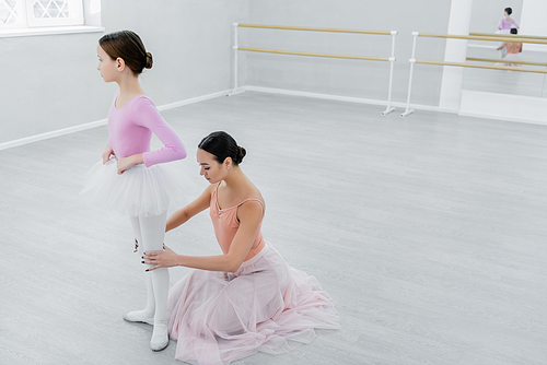 ballet master touching knees of girl during rehearsal in dancing hall