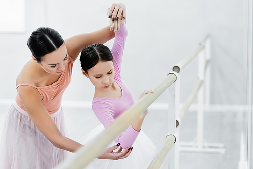 ballet master teaching girl at barre on blurred foreground