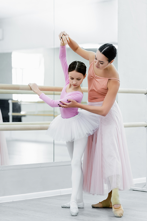 full length view of girl training in ballet school near young dance teacher