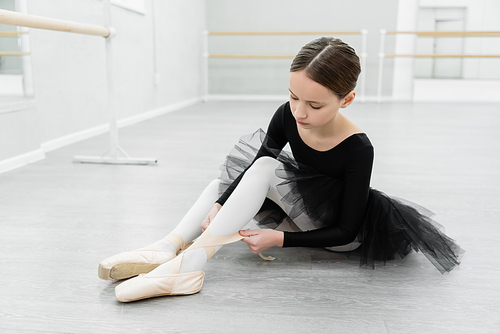 girl sitting on floor in dancing hall and tying pointe shoe