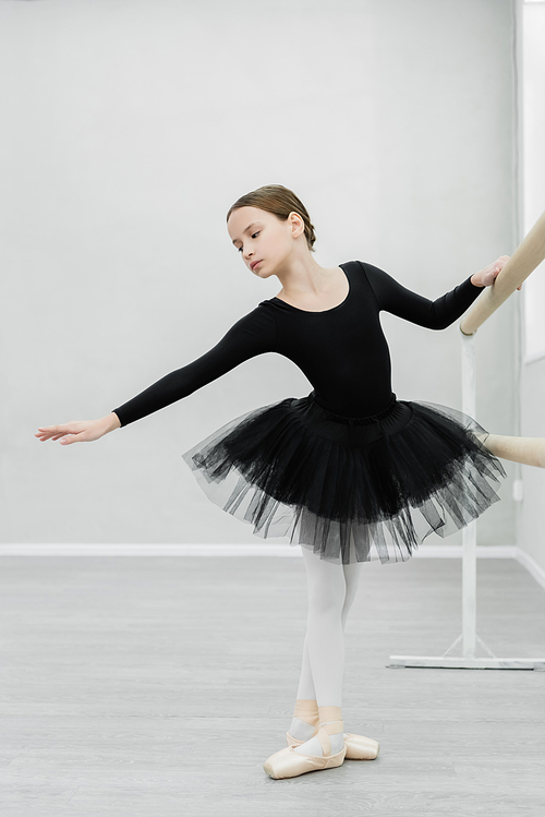 full length view of graceful girl in black ballet costume training in dancing hall