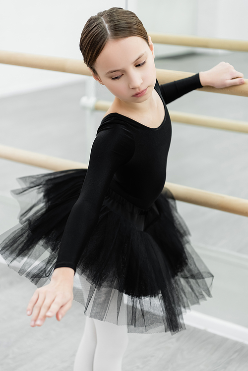 preteen girl in black ballet costume exercising at barre in studio