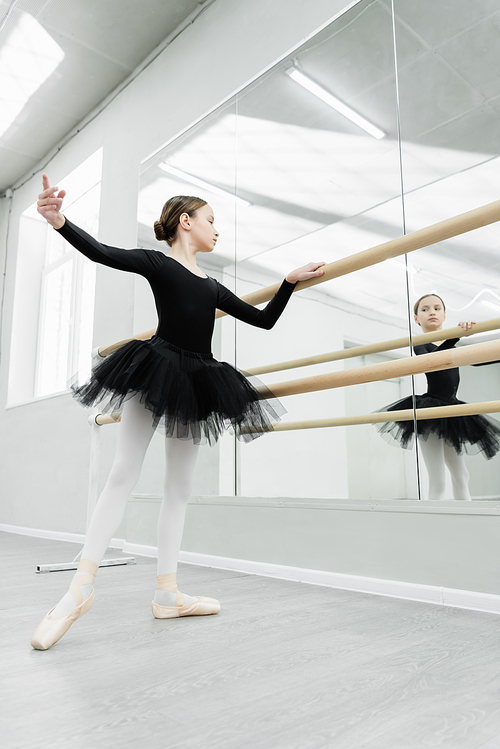 child in black tutu looking in mirror during repetition in ballet studio