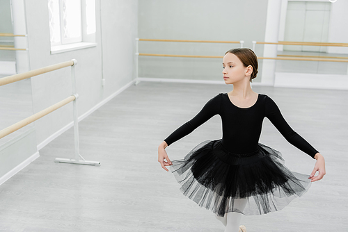 girl in black ballet costume making curtsy while training in dancing hall