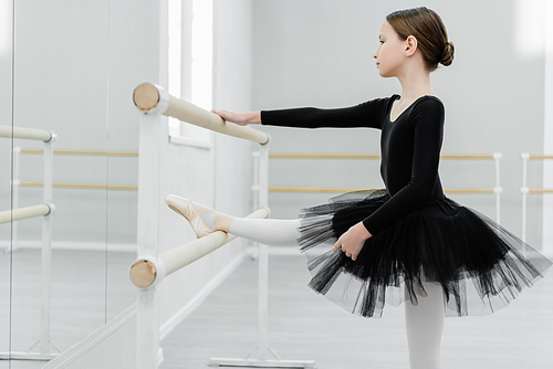 side view of kid in black tutu stretching at barre in dancing hall