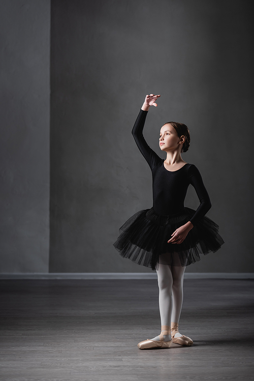full length view of girl in black tutu practicing choreographic elements in ballet studio