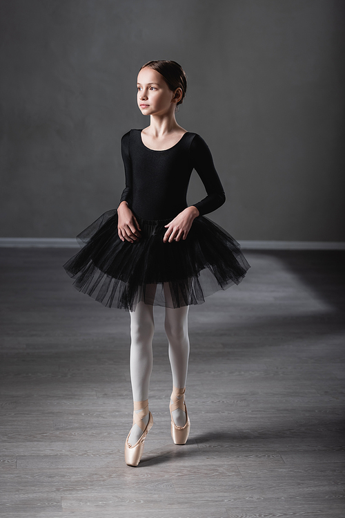 preteen girl in black tutu and pointe shoes standing on toe while training in studio