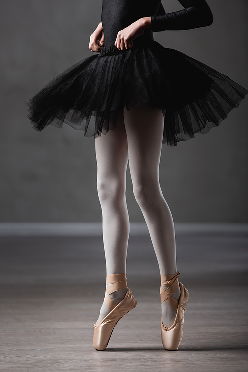 cropped view of girl in black tutu and pointe shoes dancing in ballet studio