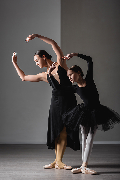 full length view of girl in black tutu training near graceful ballet teacher