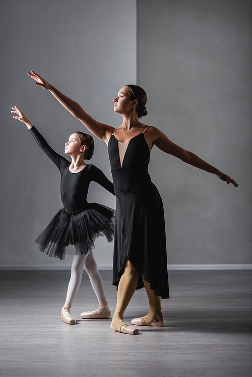 full length view of ballet teacher and girl in black tutu dancing during lesson