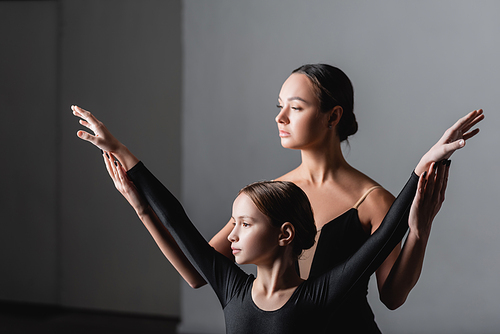 young ballet teacher raising hands of girl during dance lesson