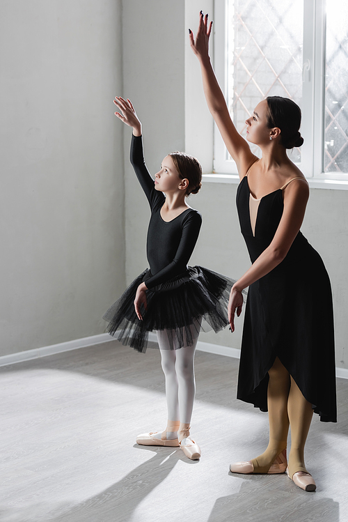 full length view of girl learning to dance ballet near graceful ballerina