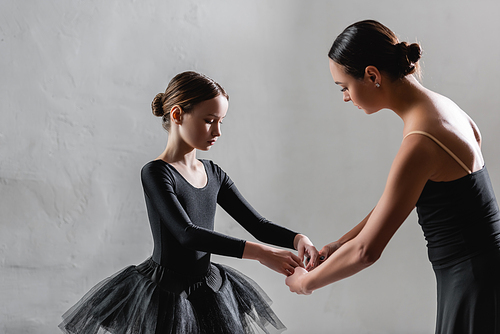 ballet teacher showing choreographic element to girl in black tutu on grey background