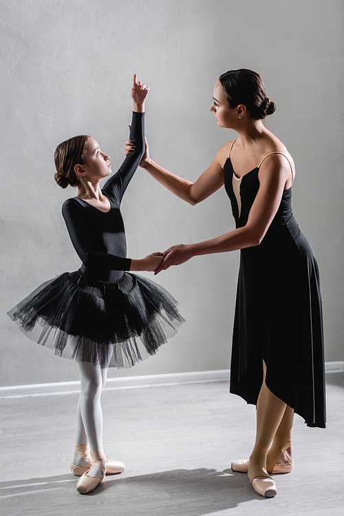 full length view of ballerina teaching girl to dance ballet in studio