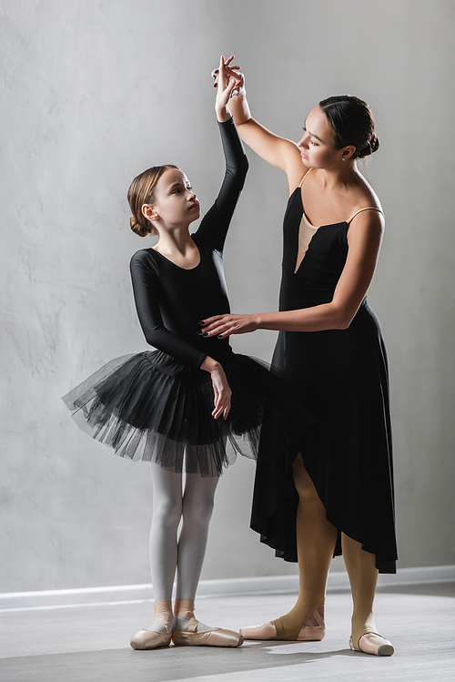 graceful ballerina raising hand of girl learning to dance ballet