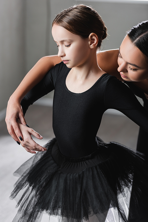 ballet teacher holding hand of girl in black tutu during dance lesson