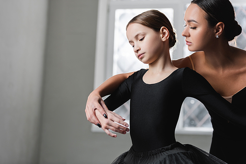 young ballerina assisting girl learning to dance ballet