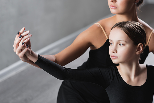 ballet teacher holding hand of girl during dance lesson