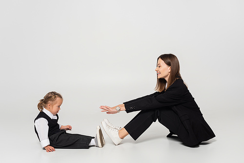 side view of cheerful mother sitting and reaching child with down syndrome on grey