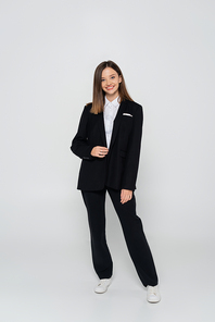 full length of happy and stylish woman in suit on grey