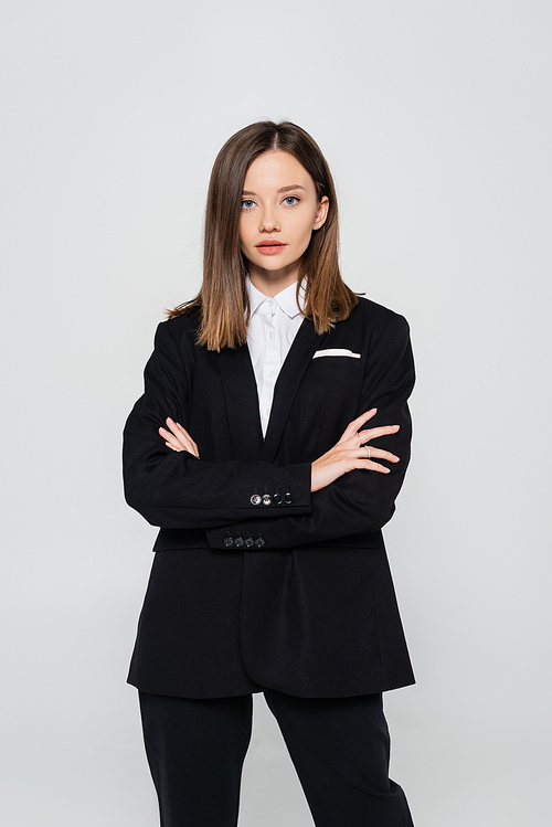 stylish woman in suit standing with crossed arms isolated on grey