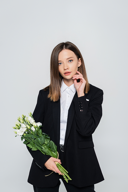 trendy woman in black suit holding flowers isolated on grey