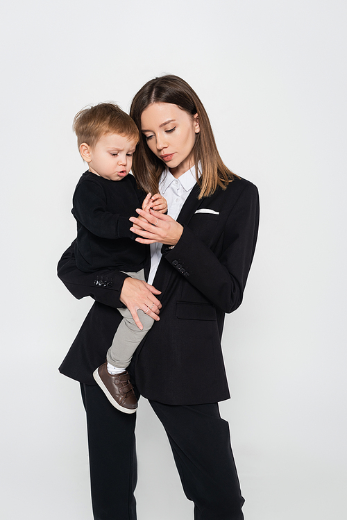stylish mother in suit holding in arms toddler son isolated on grey