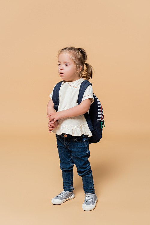 girl with down syndrome standing with backpack on beige