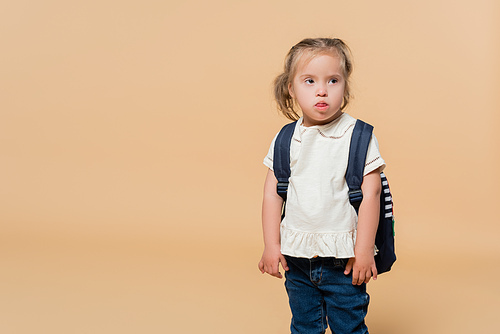 kid with down syndrome sticking out tongue while standing with backpack on beige