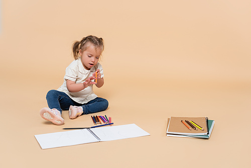 child with down syndrome sitting near colorful pencils on beige