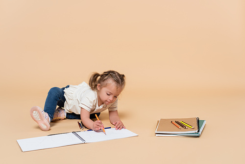 girl with down syndrome drawing near colorful pencils and backpack on beige