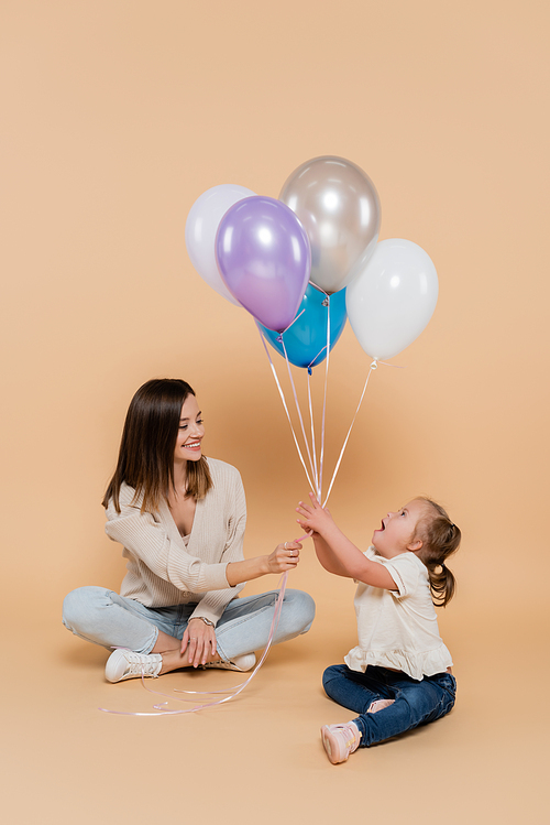 positive woman giving colorful balloons to girl with down syndrome on beige