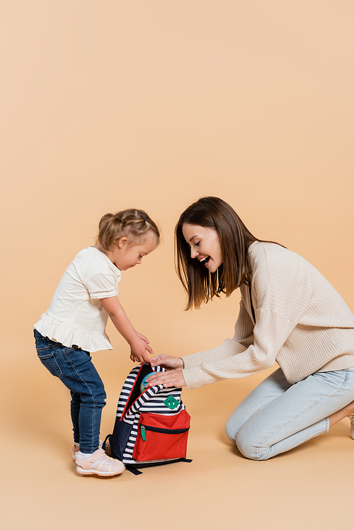 girl with down syndrome and excited mother looking at backpack on beige