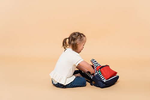 kid with down syndrome sitting with backpack on beige