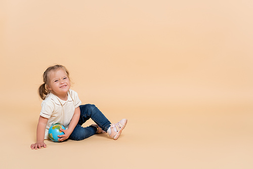 happy kid with down syndrome sitting with small globe on beige