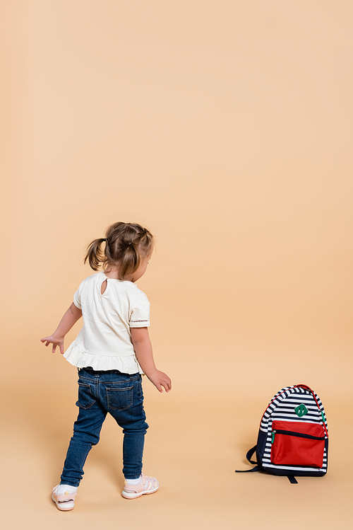 kid with down syndrome walking near backpack on beige