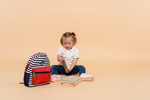 kid with down syndrome sitting near books and backpack on beige
