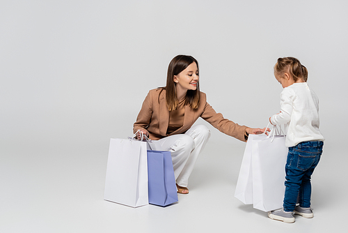 happy and stylish mother holding shopping bags near girl with down syndrome on grey
