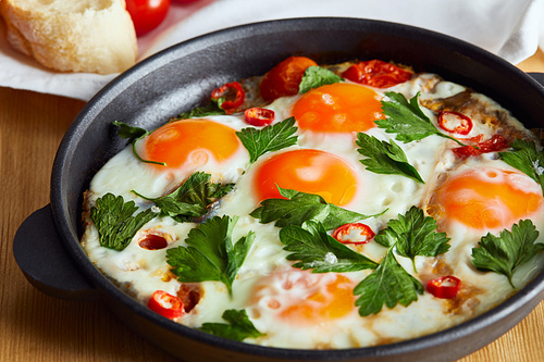 close up view of fried eggs with parsley and chili pepper in pan on wooden table