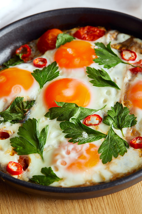 close up view of fried eggs with parsley and chili pepper in pan on wooden table